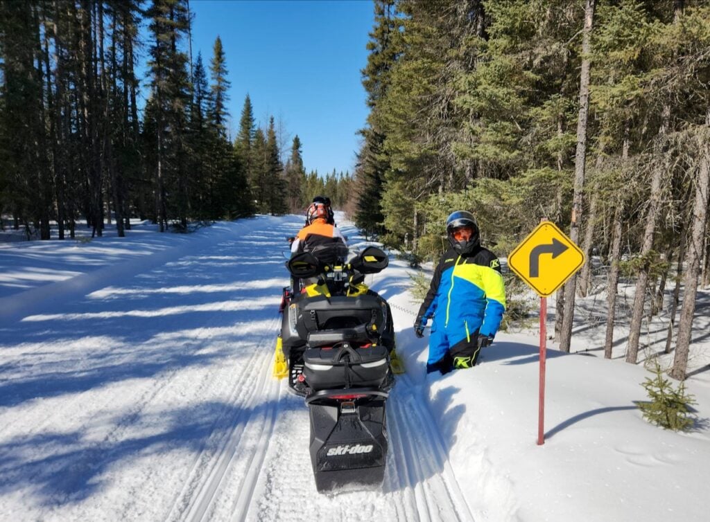 Man standing on the edge of a snowmobile trail showing the depth of snow on the ground